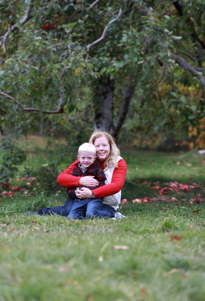 mom and son sitting under an apple tree, mom hugging son from behind, apples around them
