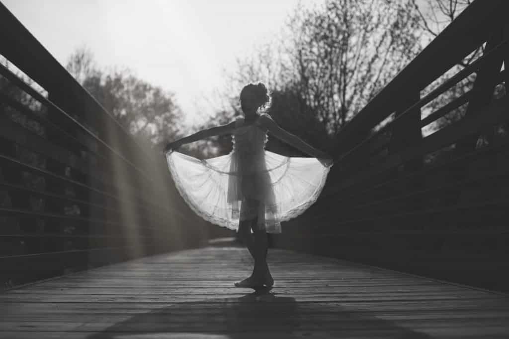 Young white girl dancing on a bridge holding her dress out in black and white