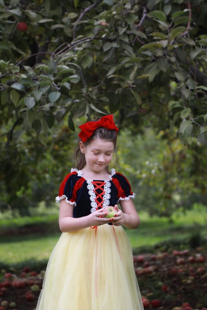 Little girl dressed up as snow white holding a red apple looking down happily at the apple
