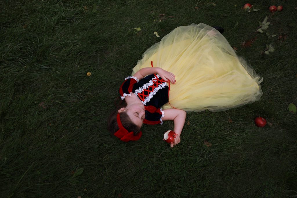 Little girl laying in grass holding a bitten red apple pretending to sleep