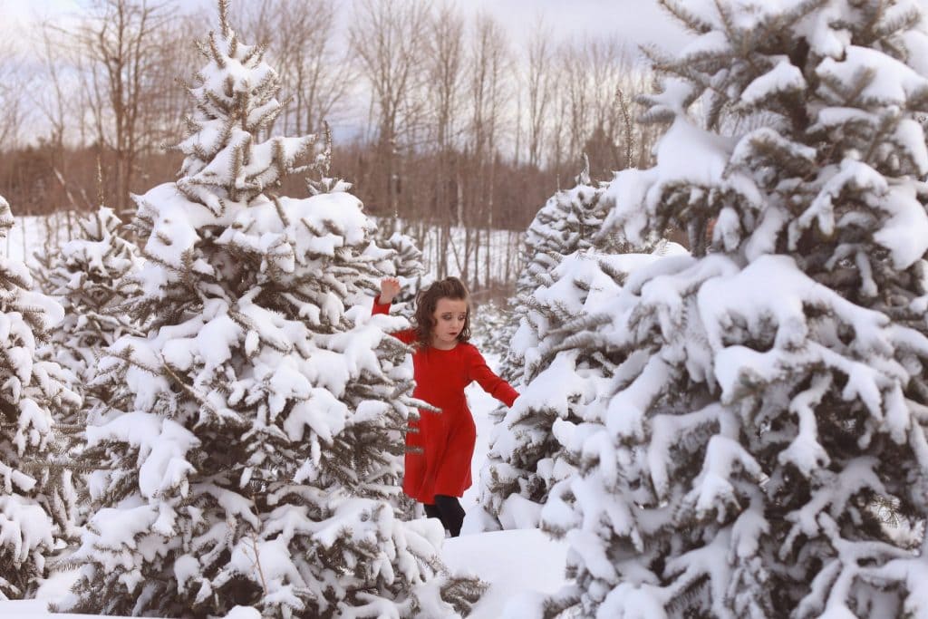 snow covered trees, tree farm, young girl, red dress, almost falling, hands in the air, mouth open, curly hair, hair half up and half down