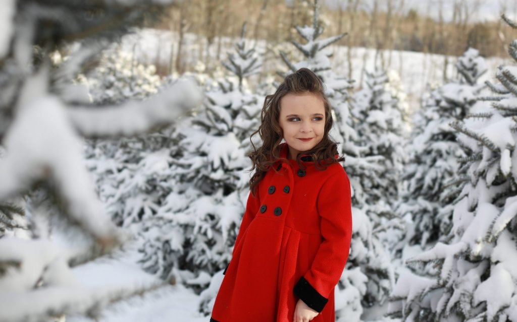 young girl, red dress, looking at mother, tree farm, snow covered trees, winter, red coat, curly hair, smiling.