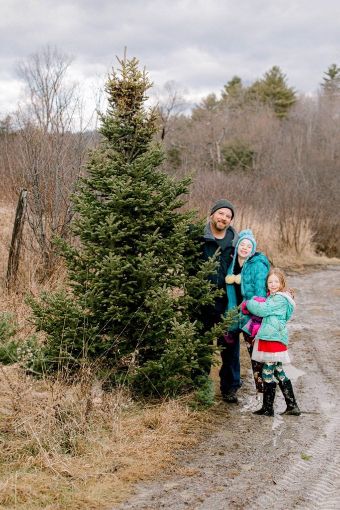 Dad, his girls looking at the camera holding the freshly cut christmas tree