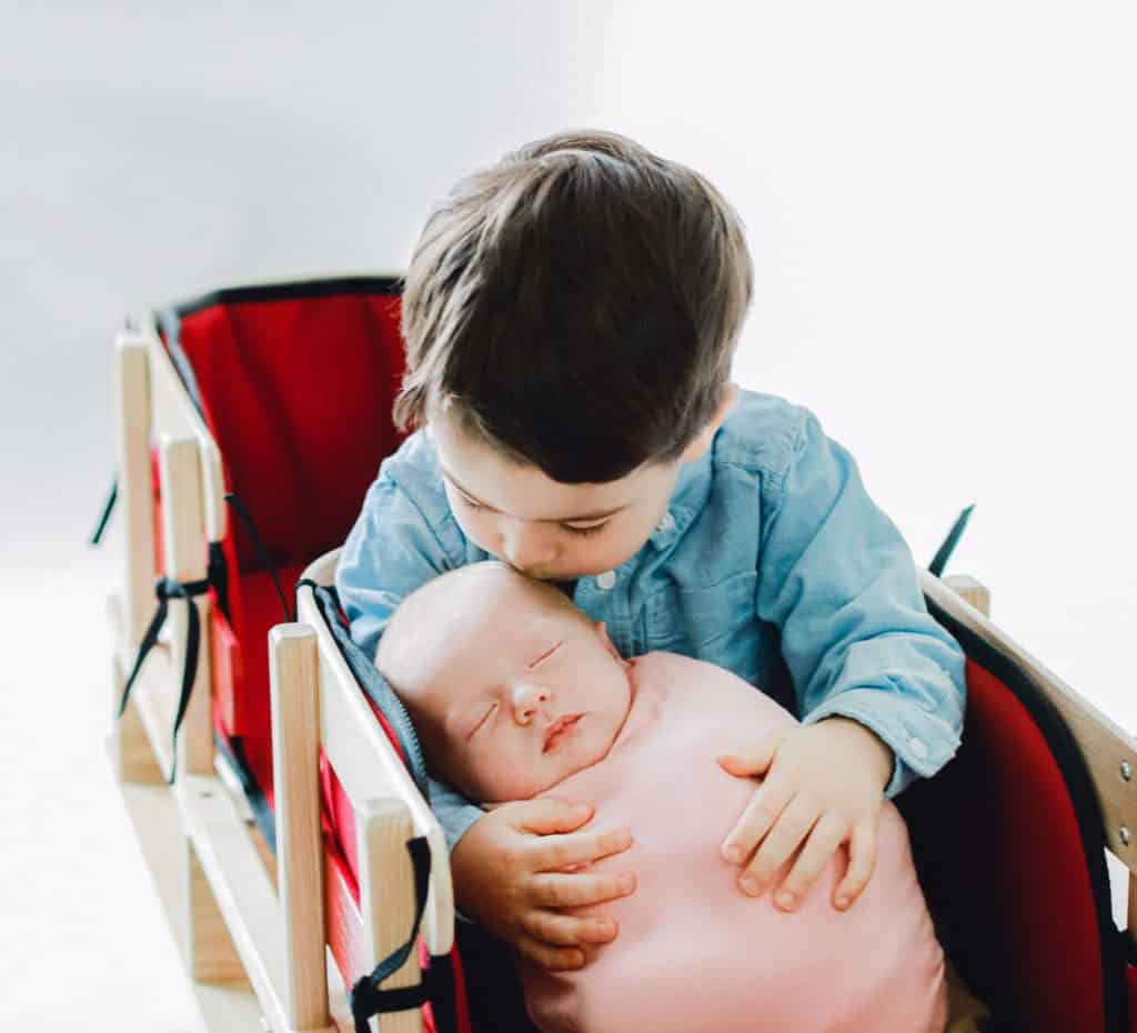big brother kissing newborn baby girl in a red double sled