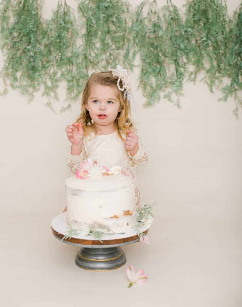One year old girl looking at the camera with a white cake mouth open