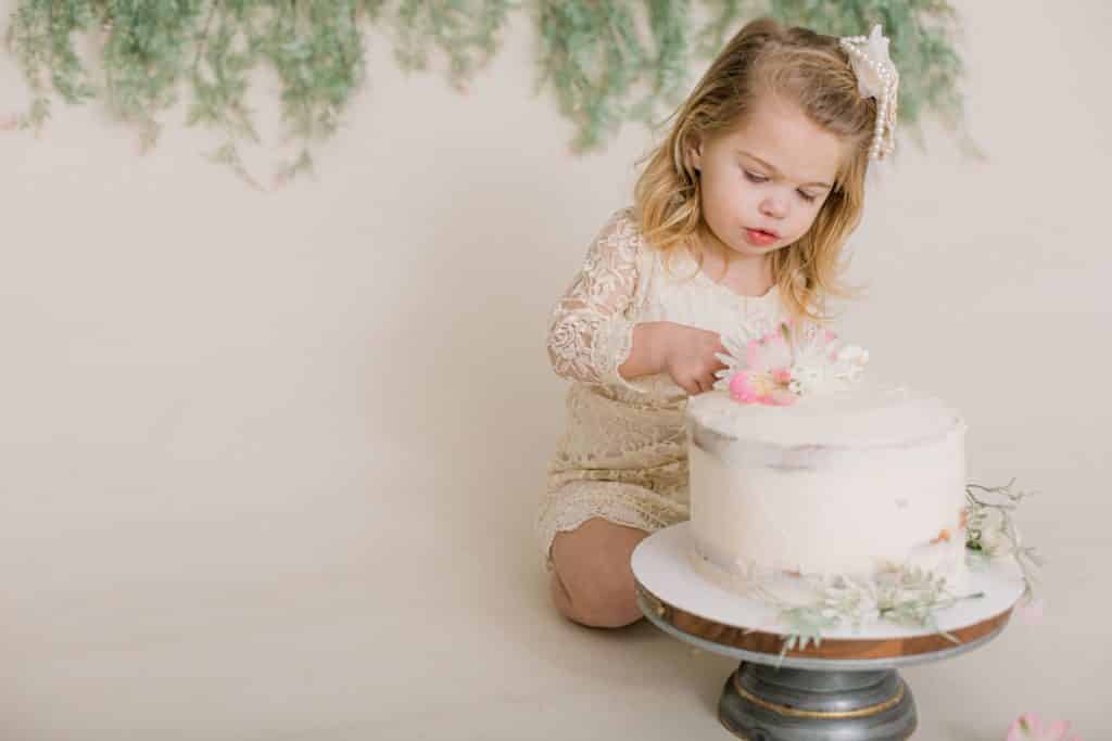 One year old girl looking at and poking her cake 