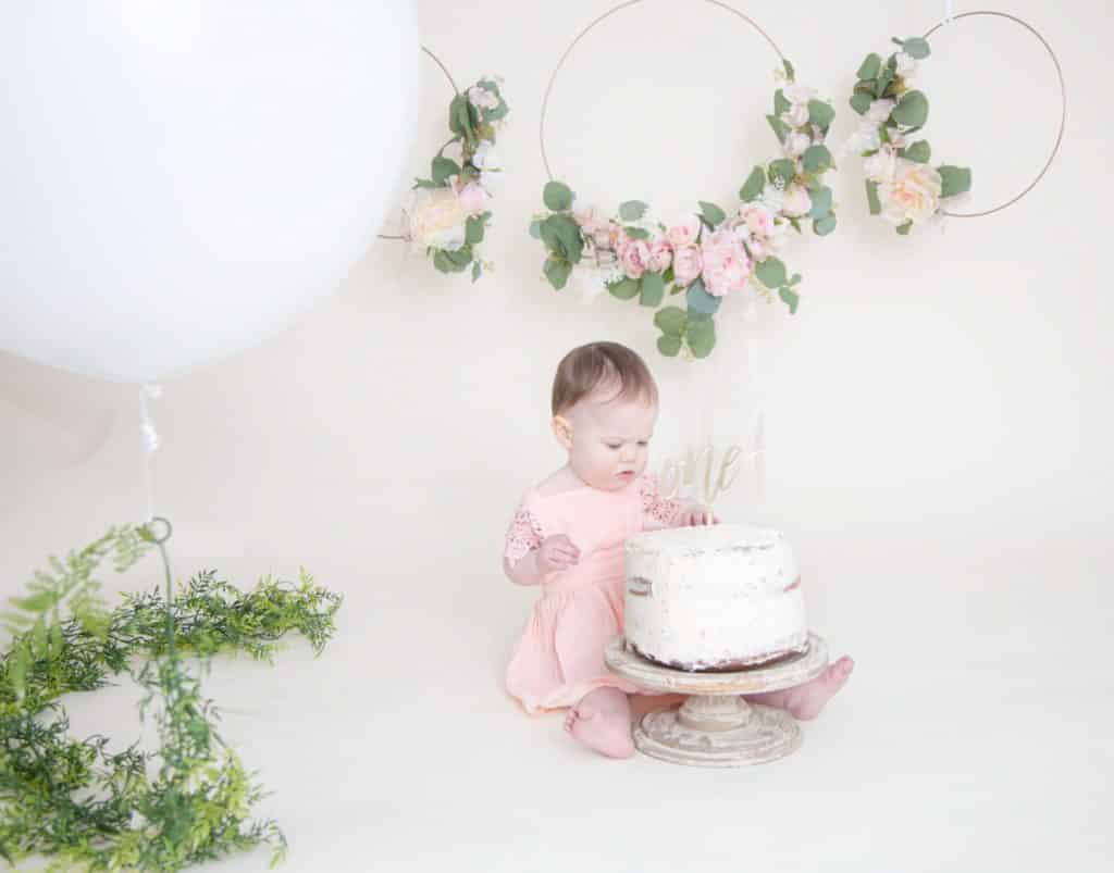 one year girl looking at the cake with a pink dress and white balloon