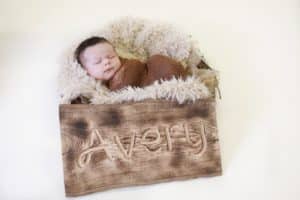 Newborn boy laying in next basket with a name sign and burlap