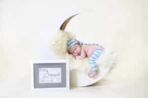 newborn baby boy in blue laying in a moon with personalized sign