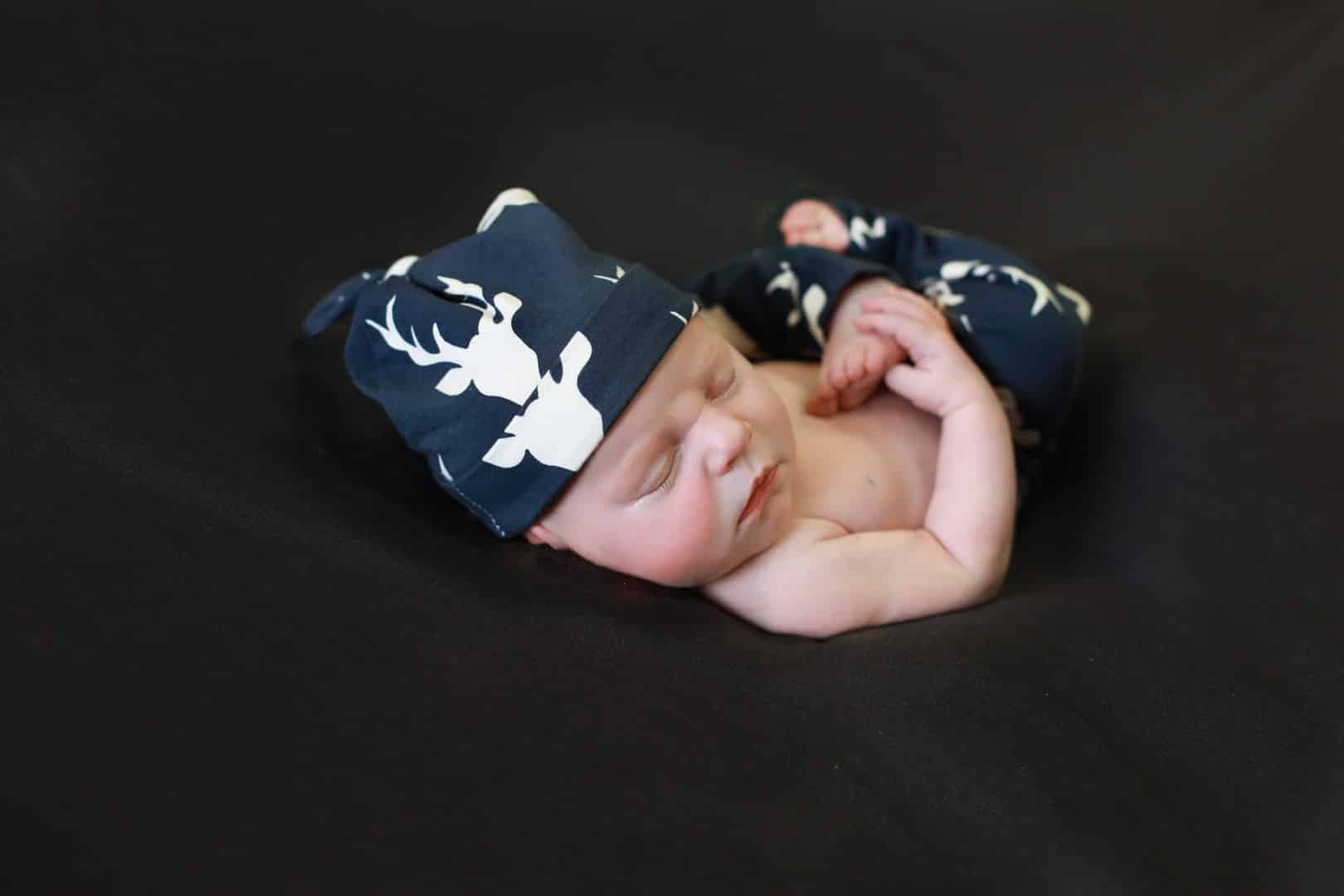 baby sleeping, grabbing foot, navy blue deer hat and pants