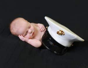 newborn baby sleeping on side, black background, covered with military white and black marine hat