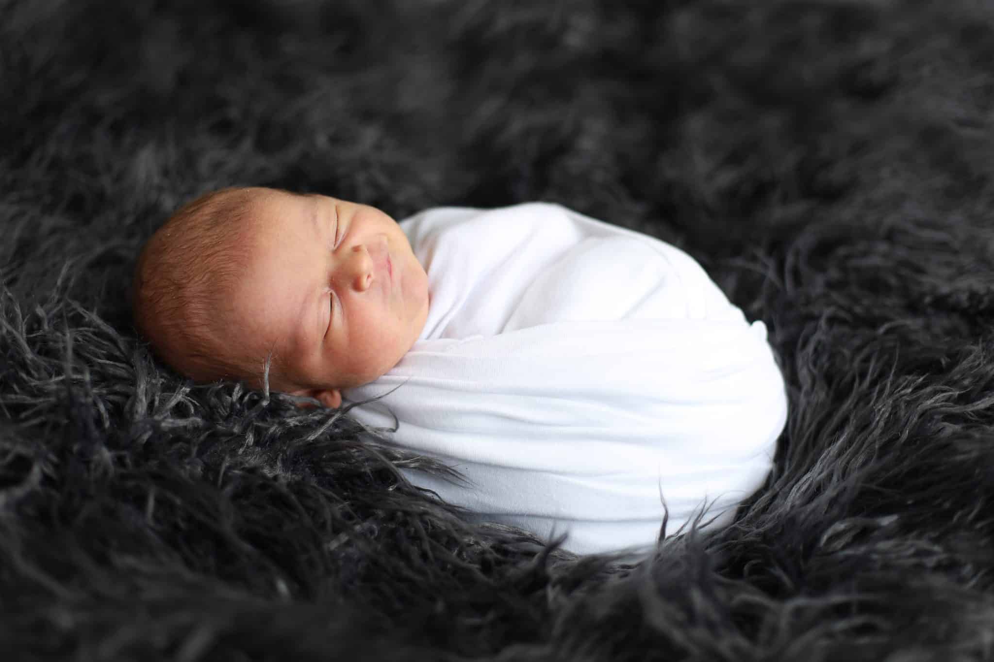 baby wrapped in white wrap on greay fur sleeping