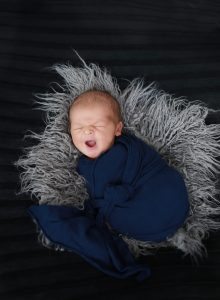 newborn wrapped in blue wrap on grey fur and black background yawning