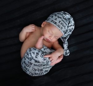 newborn baby in a grey love outfit curled up on a black background with a gray hat