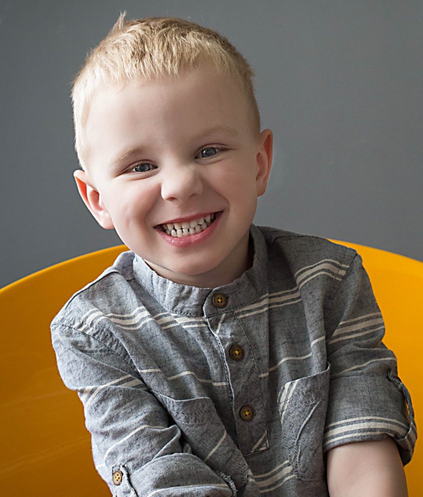 oldest son sitting in yellow chair, smiling big at the camera