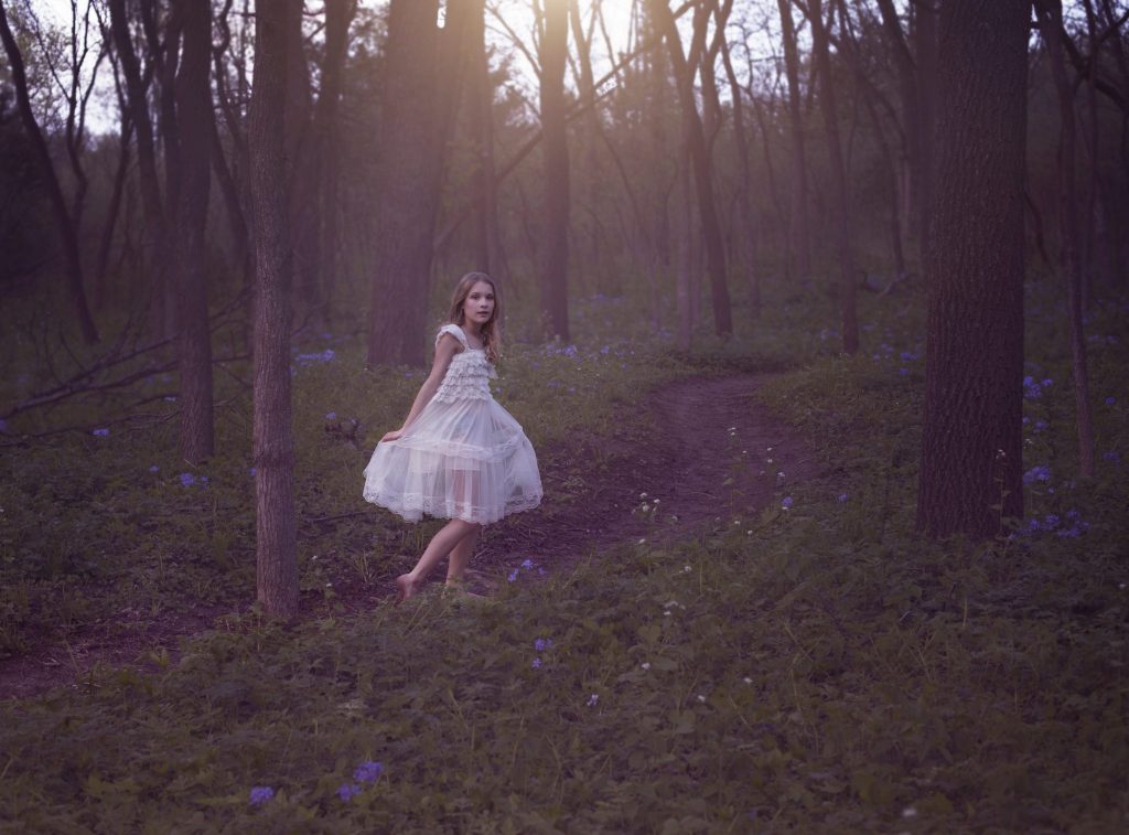 Young white girl running through the woods at dusk 