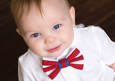 one year old boy in white shirt and red boytie, sitting on hardwood floor