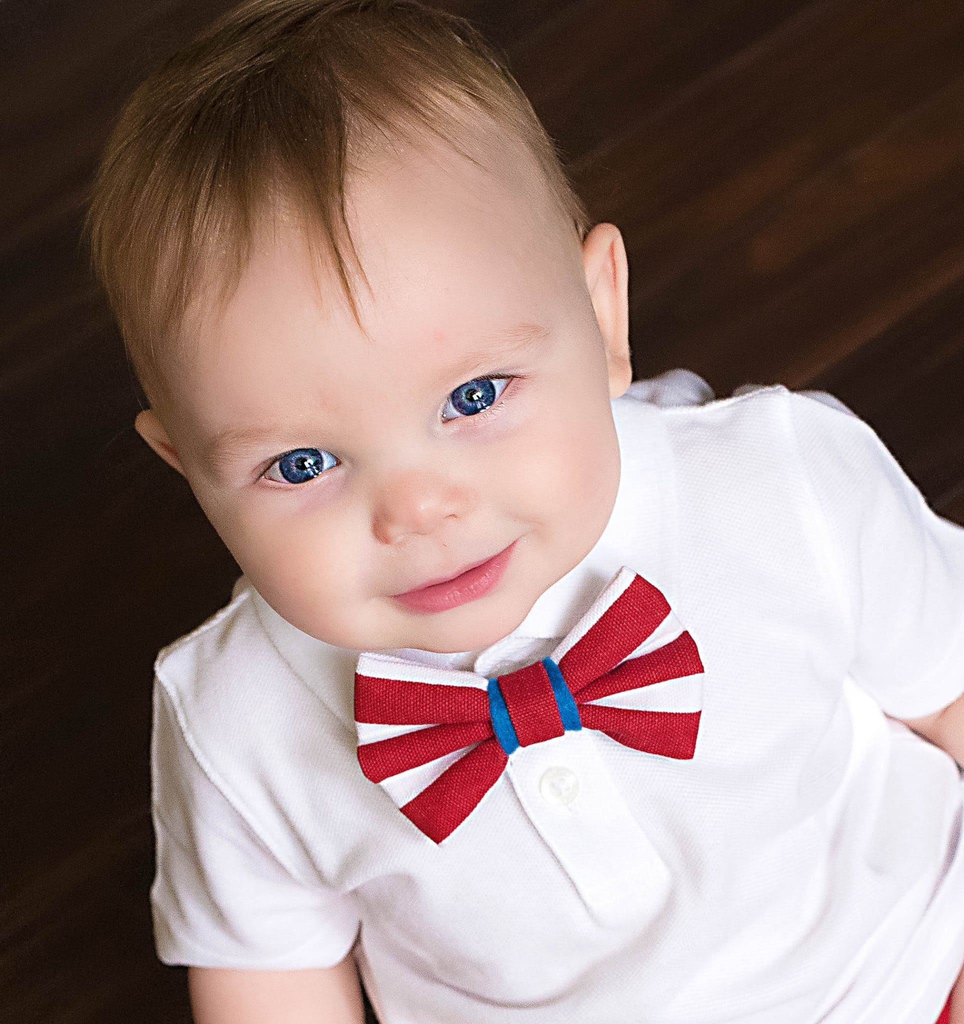 one year old boy in white shirt and red boytie, sitting on hardwood floor