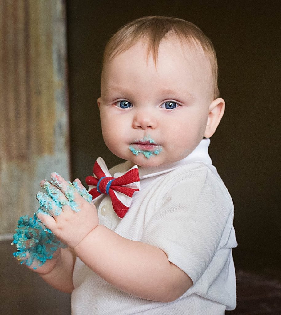 One year old looking at camera with cake hands