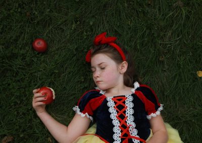 little girl laying on grass dressed up as snow white, holding a bitten apple with her eyes closed.