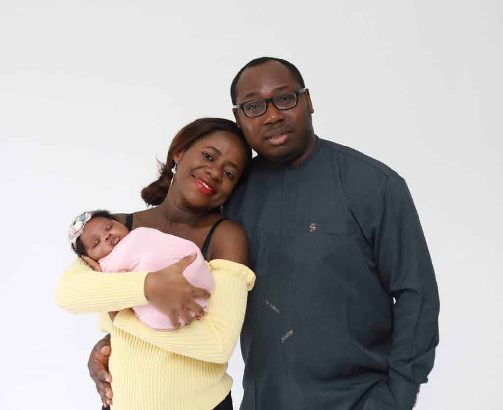 dad holding mom looking at camera, mom holding newborn looking at camera both smiling