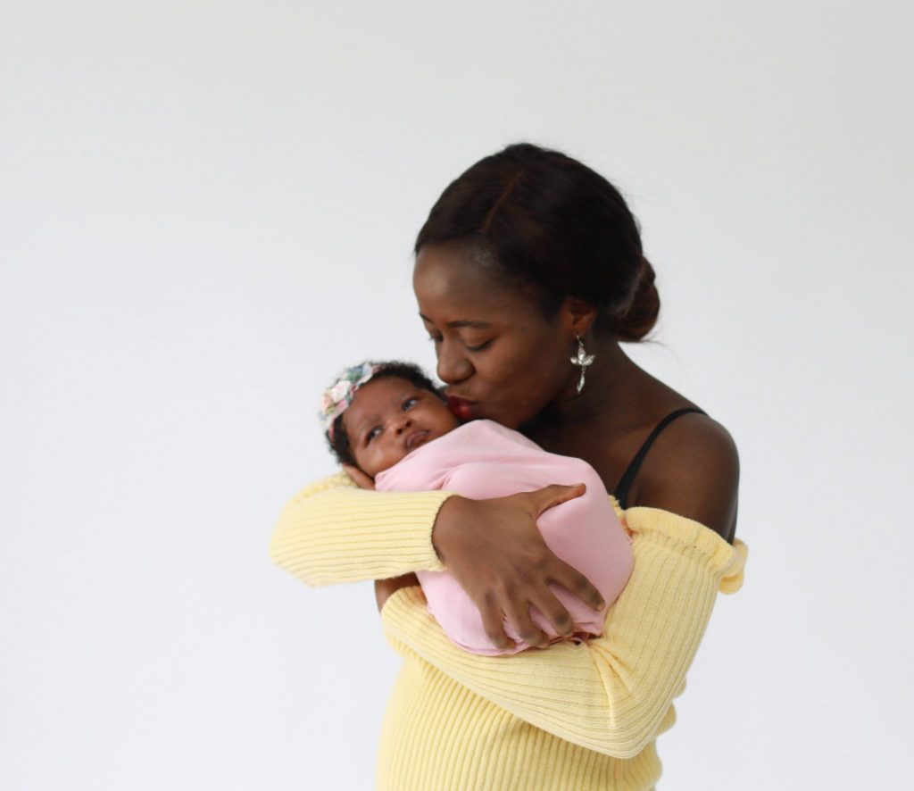 mom holding newborn girl wrapped in pink kissing her