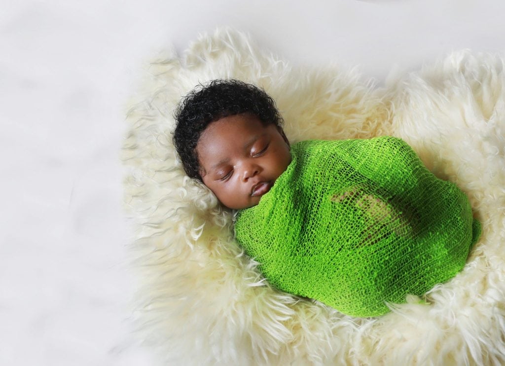 newborn girl wrapped in green wrap, on white fur