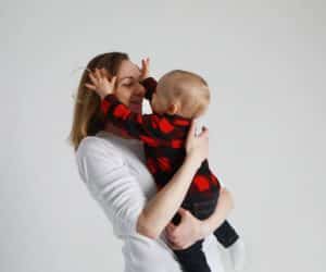 One year boy with red and black plaid sweater and jeans being held by his mother wearing a white shirt