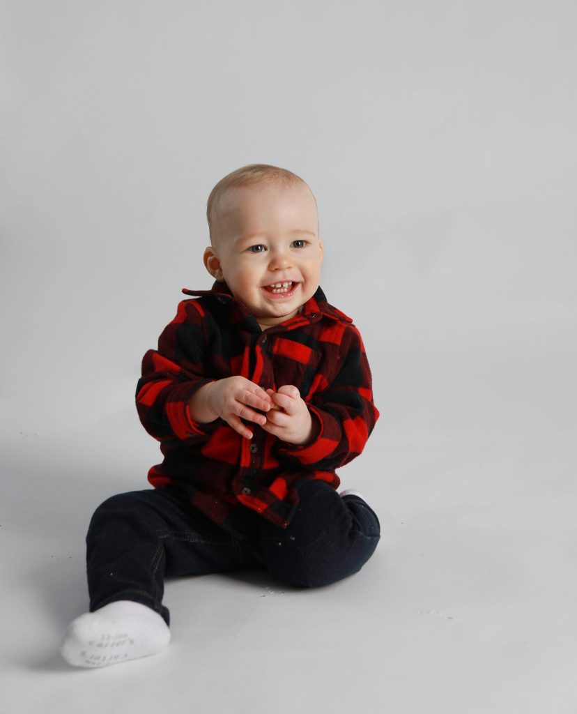 One Year boy sitting on a white background with a plaid sweater and jeans