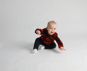 One year boy wearing red and black plain sweater on a white background playing with a number one balloon.