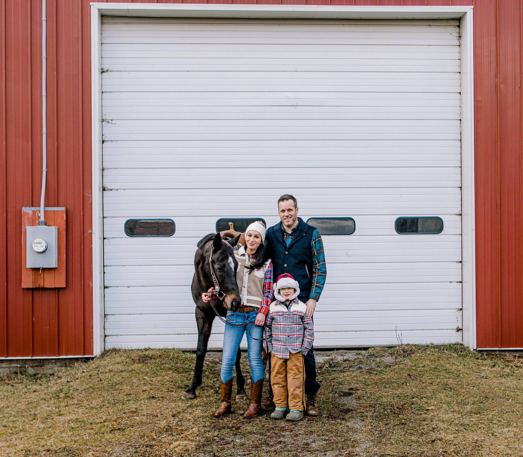 family against a white and red barn looking at the camera for their family photo