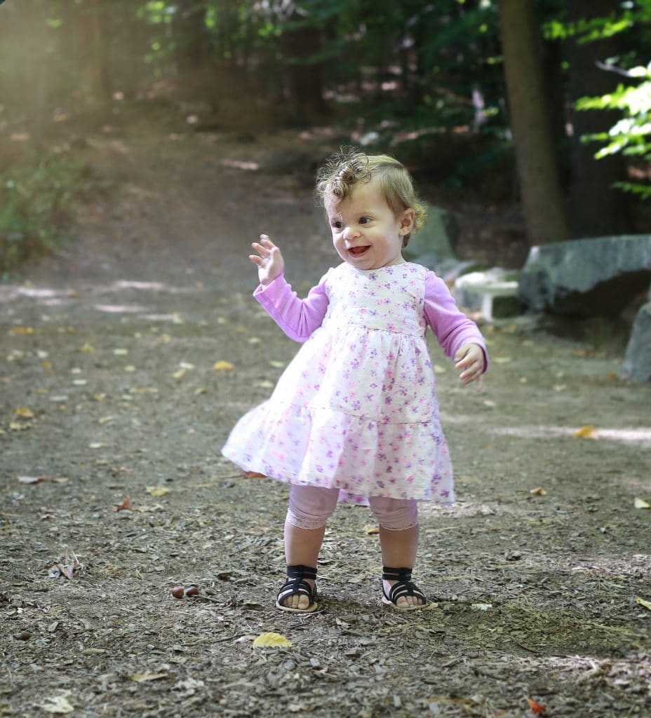 little girl dancing in pink dress on a path in the woods, hands up, curly hair