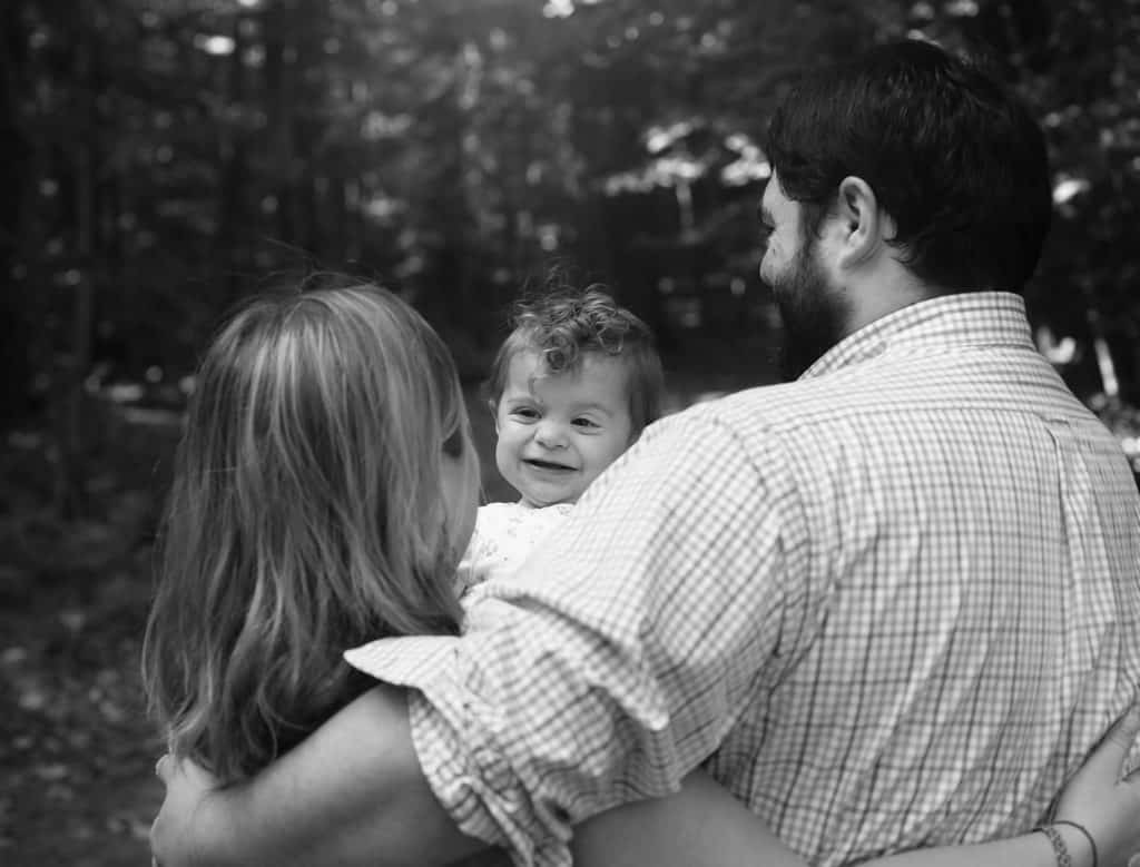 mom and dad back to the camera, baby girl smiling at mom, in black and white