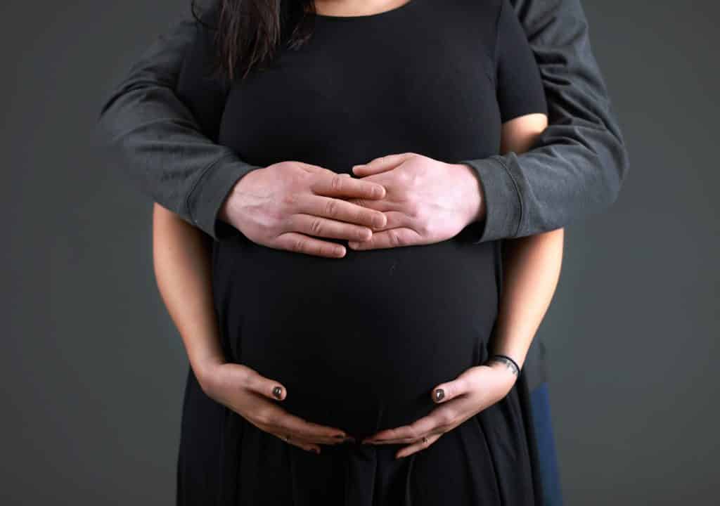 husbands hands wrapped around wife, hands on belly