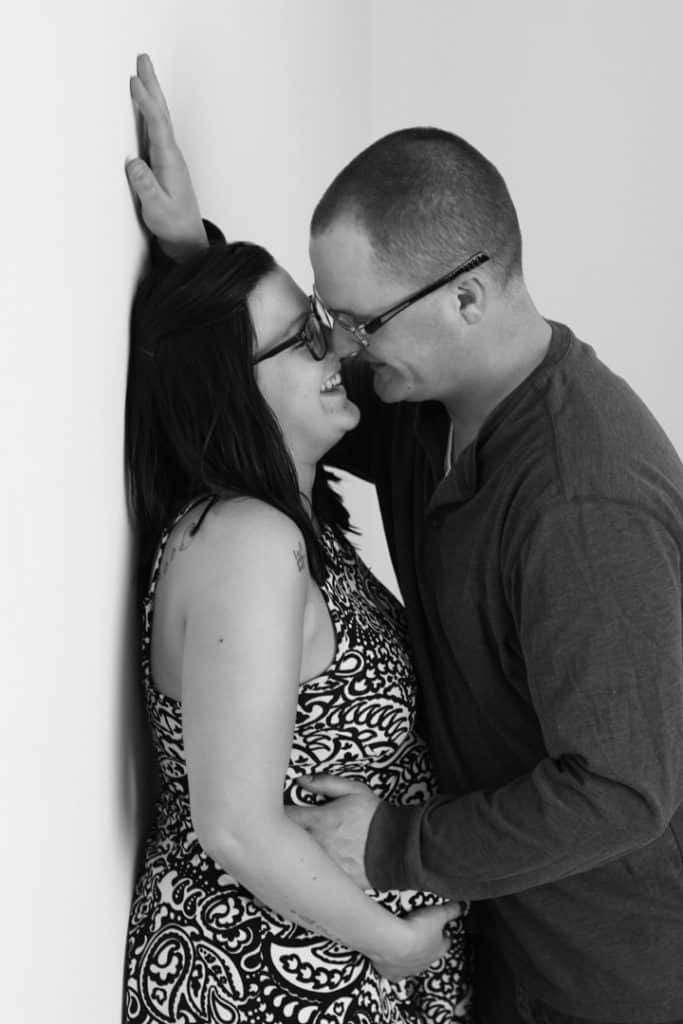 husband and wife, husband almost kissing wife against the wall, hand on her stomach