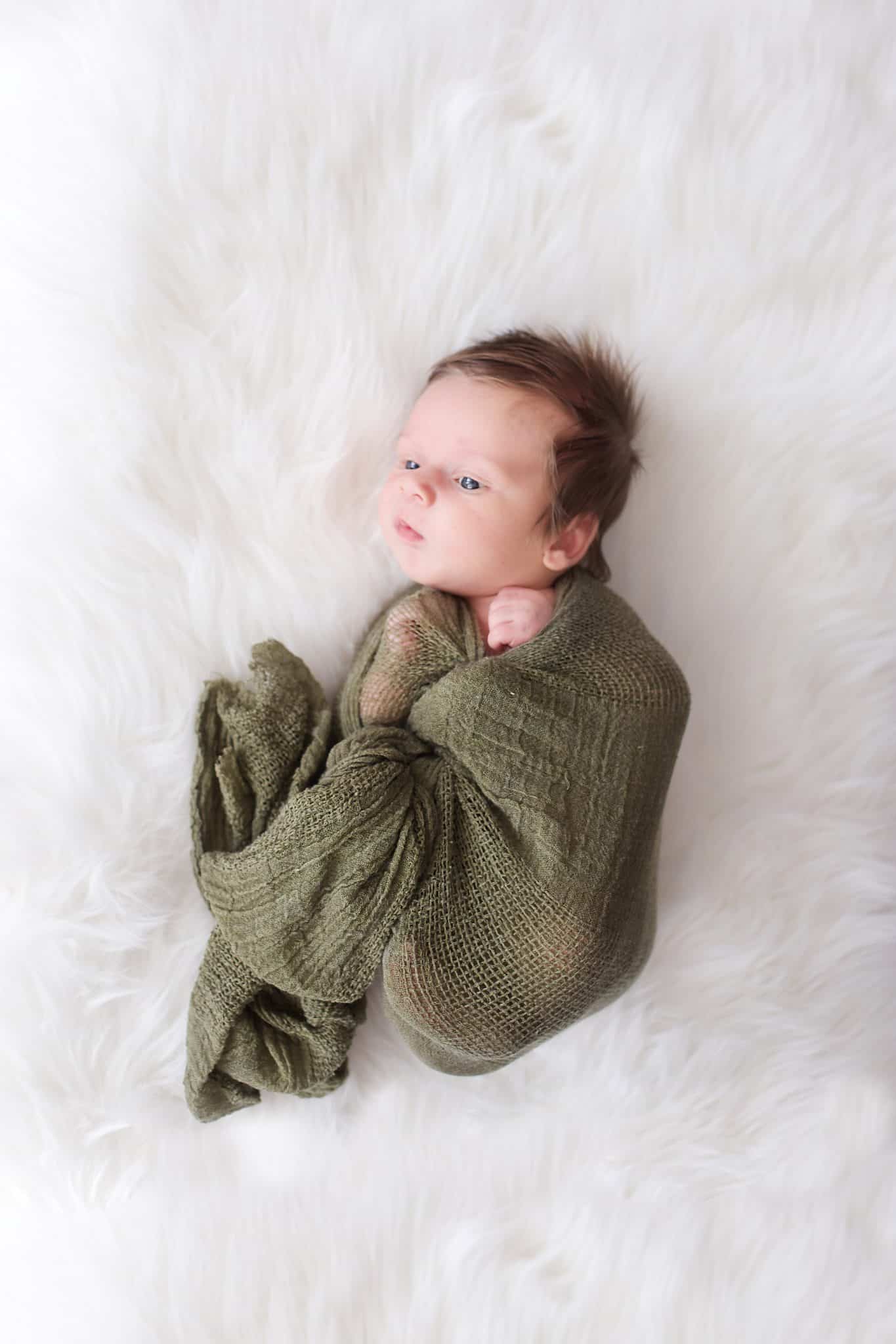 Newborn photo session. Newborn, olive green wrap, white fur blanket, tons of hair, eyes open