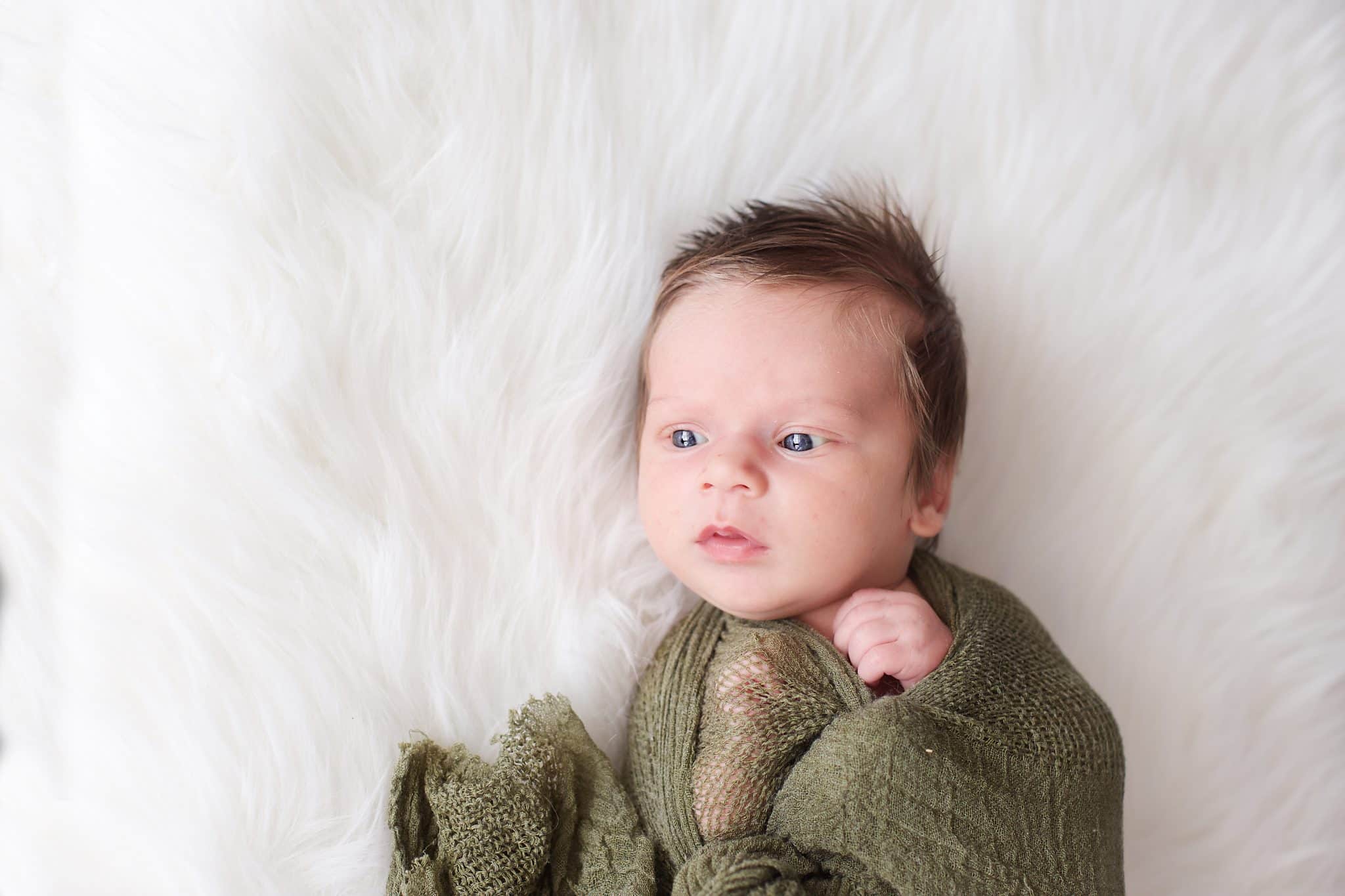 Newborn photo session. Newborn, olive green wrap, tons of hair, eyes wide open, on white fur backdrop