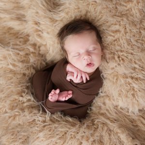 Newborn photo session brown wrap, mouth open, tons of hair, on a tan fur blacket