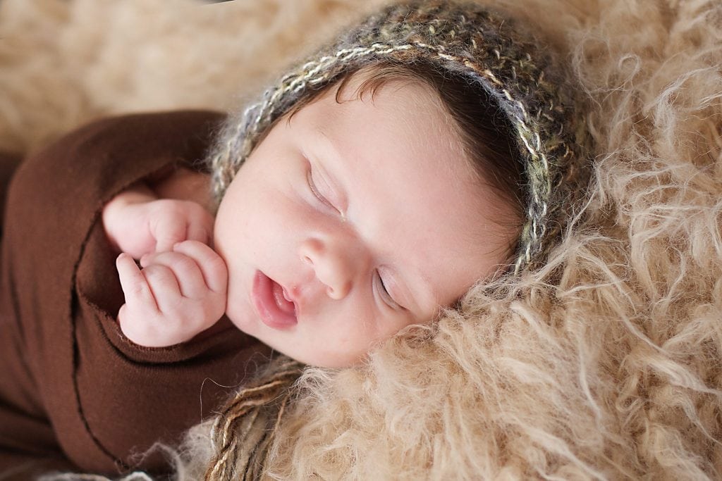 newborn in brown wrap, green bonnet, tan fur blanket, sleeping