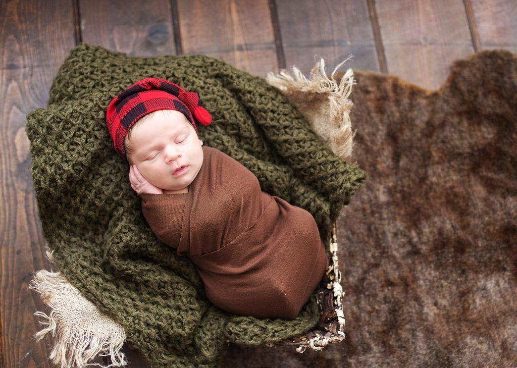 Newborn in brown wrap, burlap, basket, red plaid hat, sleeping