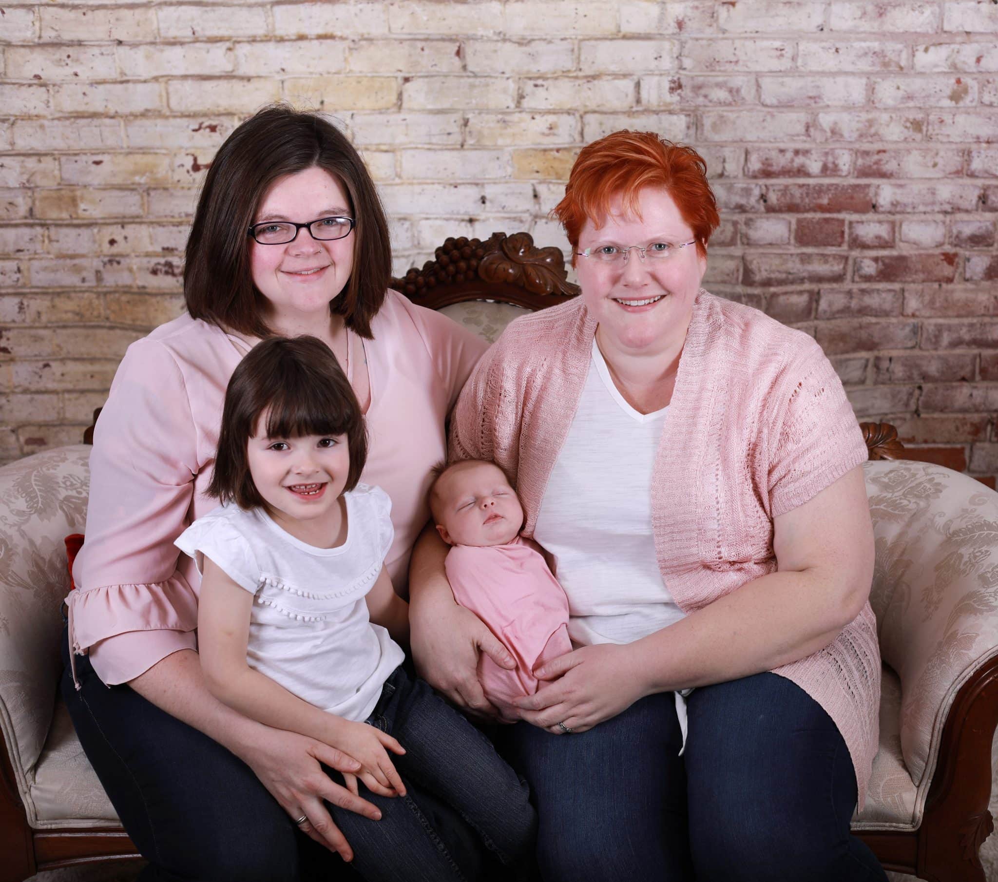 Newborn family photoshoot, pink and white clothes, sitting on a love seat, wrapped in pink