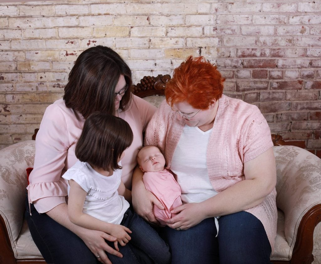 newborn family photoshoot, all wearinf jeans and pink and white, newborn wrapped in pink, all looking at newborn