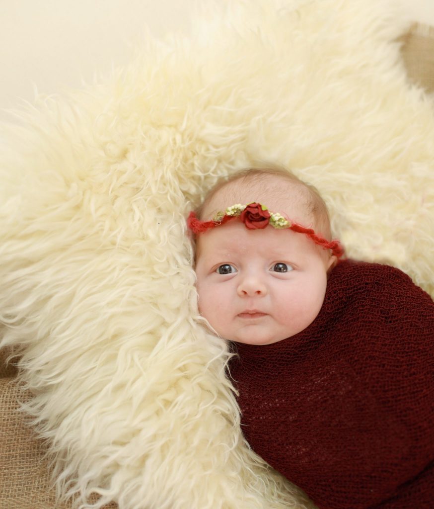 Newborn wrapped in brown, red headband with flower, off white fur