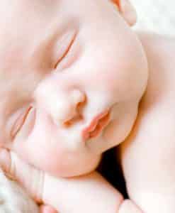 newborn baby laying on white blanket with her hands under her head facing the camera