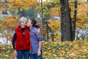grandmother and her grown grandson kissing her on the cheek in their backyard in the fall. Lifestyle images.