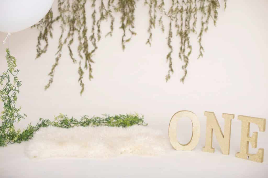 One year photo setup, white fur, a large white balloon, green garland and an off white background