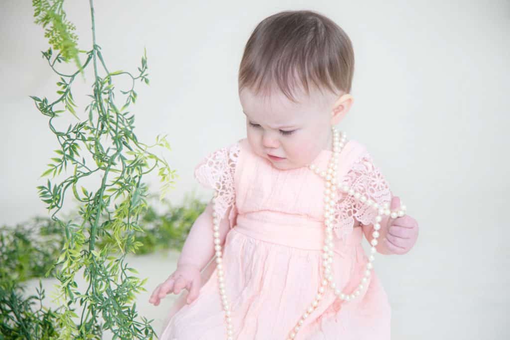 One year girl in pink dress holding pearls looking down