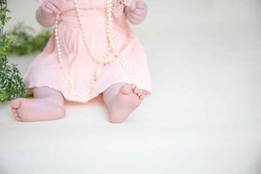 one year girl in pink dress on white background. Picture of her feet