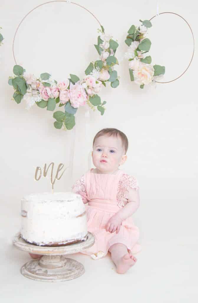 One year girl looking at the camera sitting in front of cake smash with puckered lips