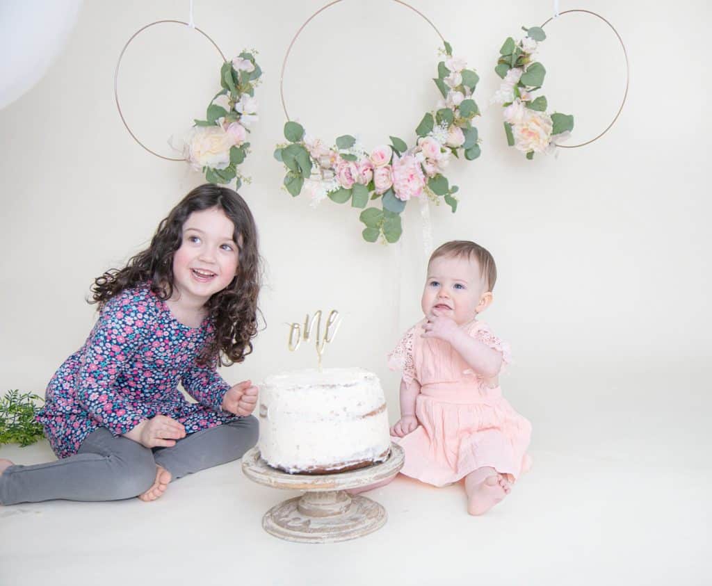 One year old and sister looking at the camera and eating cake